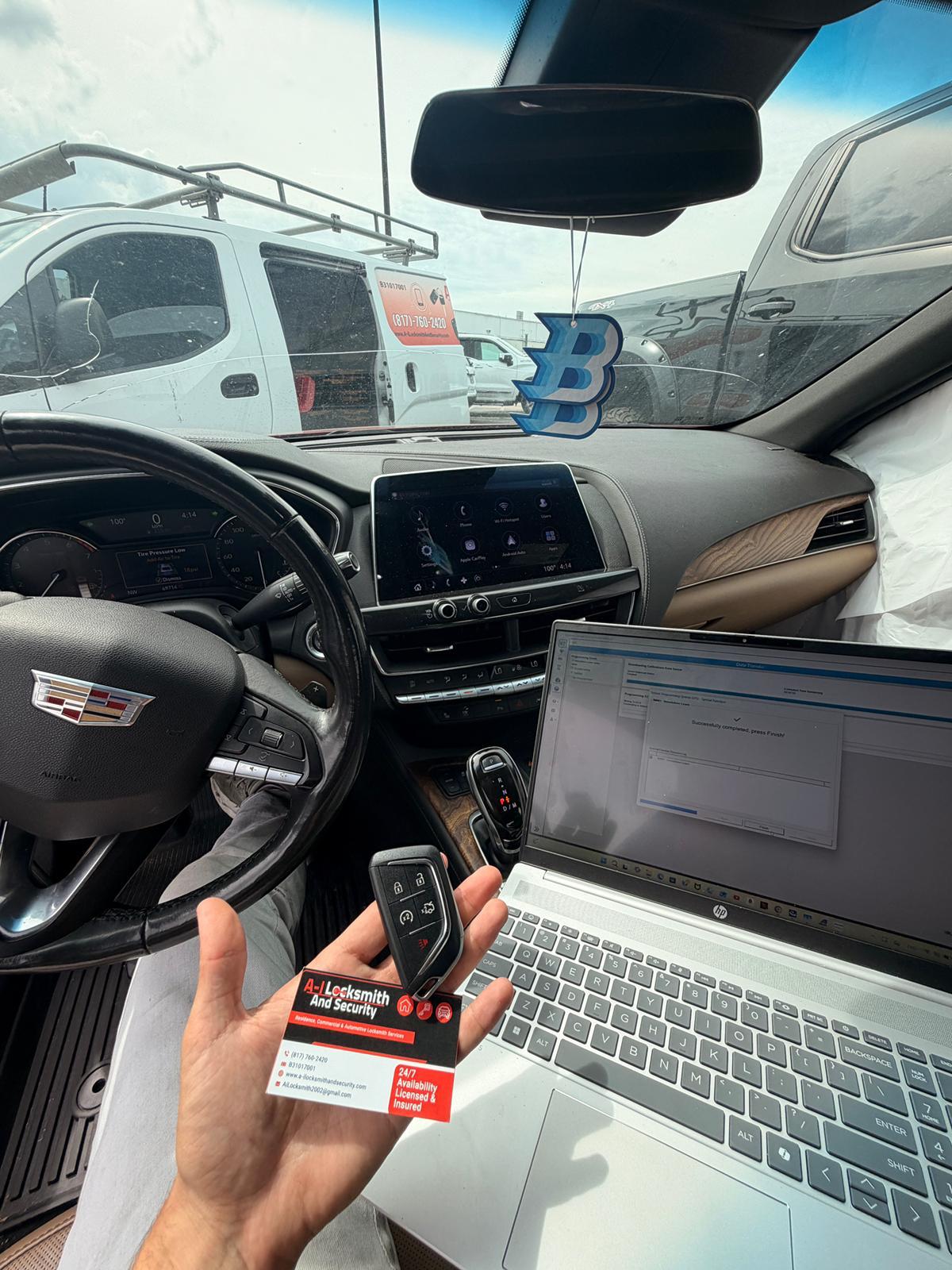 Cadillac key fob beside a programming laptop and A-I Locksmith business card