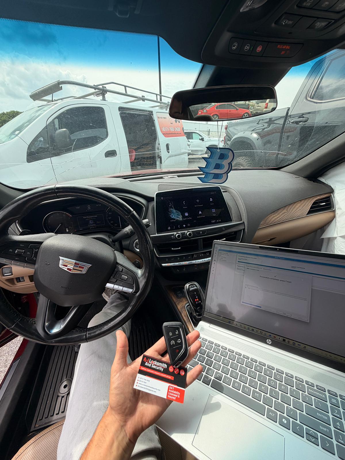 Cadillac key fob and programming laptop inside a vehicle, with the A-I service van outside