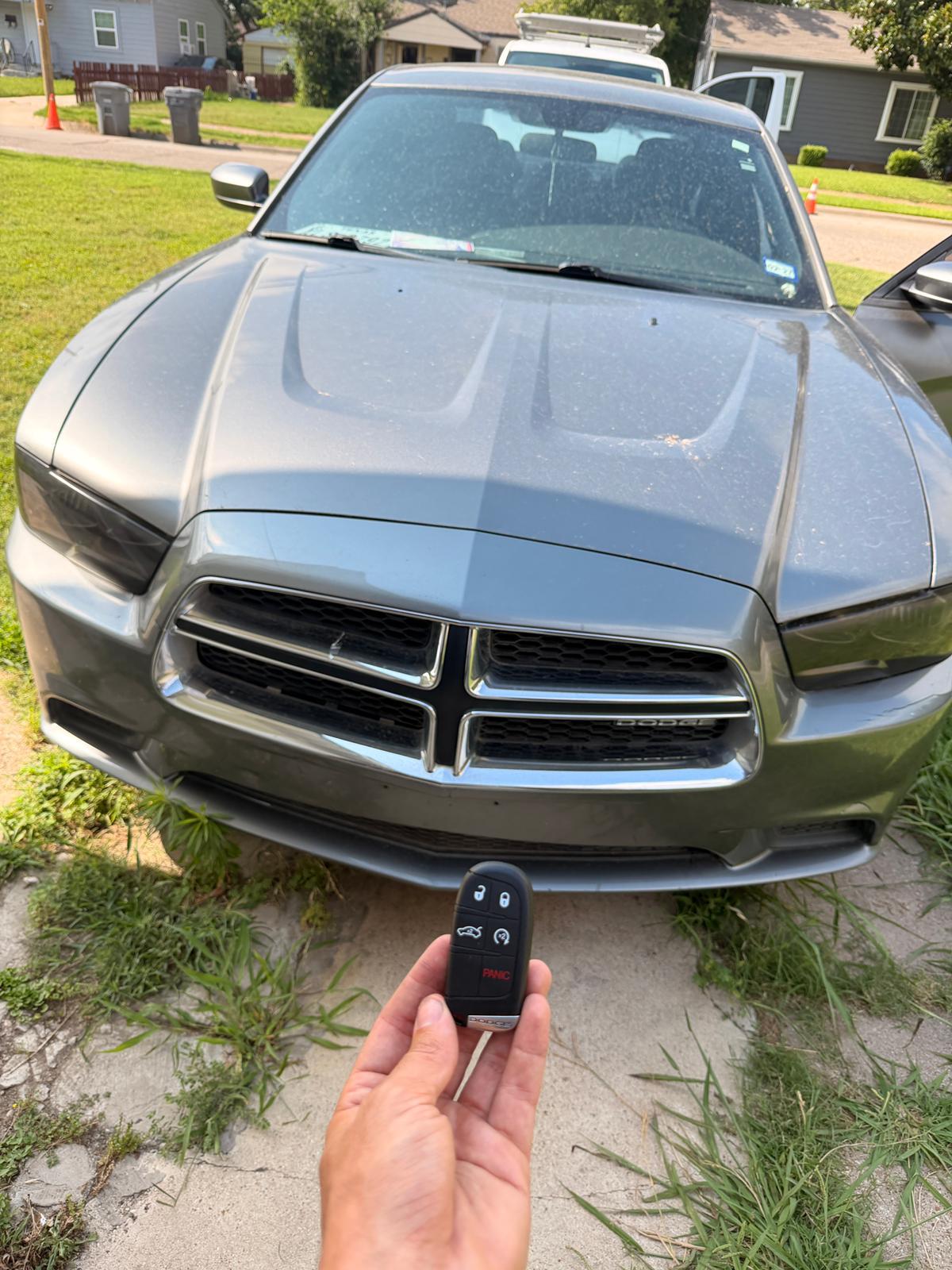 Dodge key fob held in front of a gray Dodge sedan