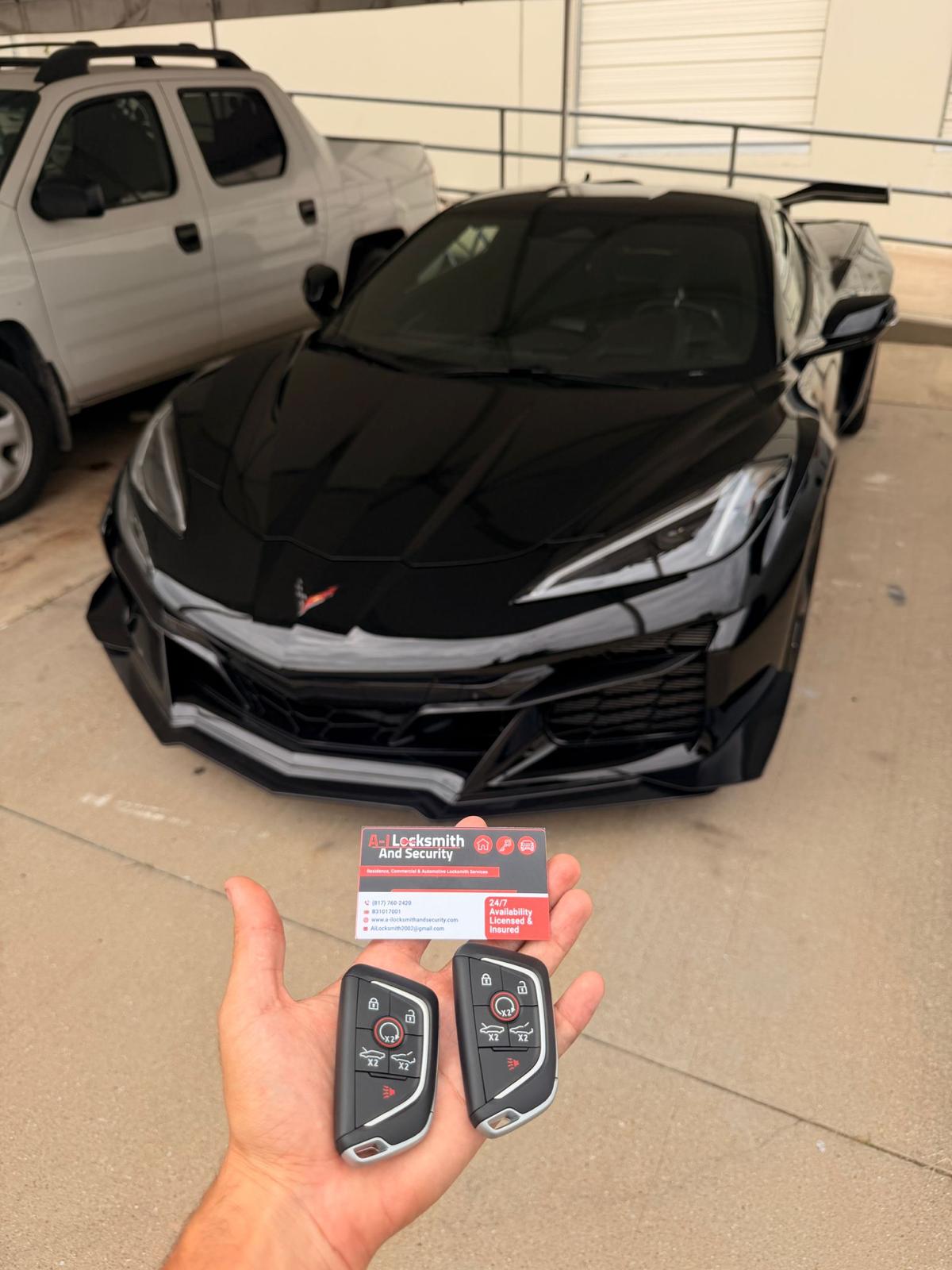 Two Corvette key fobs with a black Chevrolet Corvette and A-I Locksmith business card